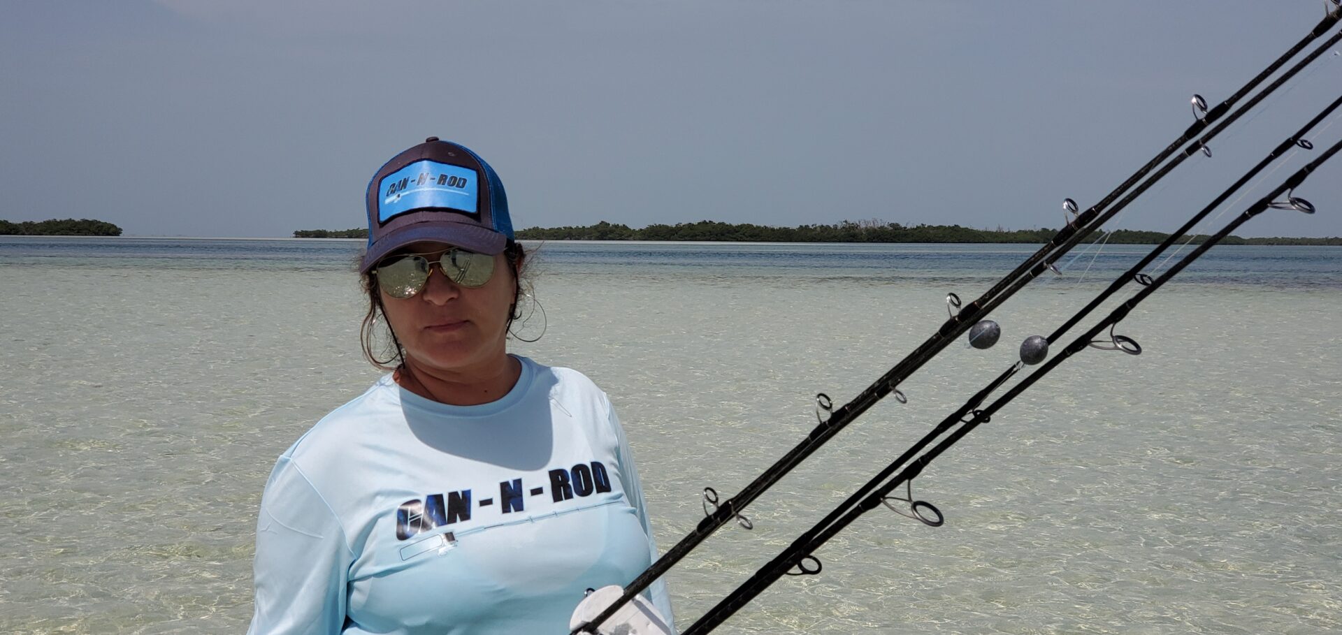 A woman holding two fishing rods on the beach.