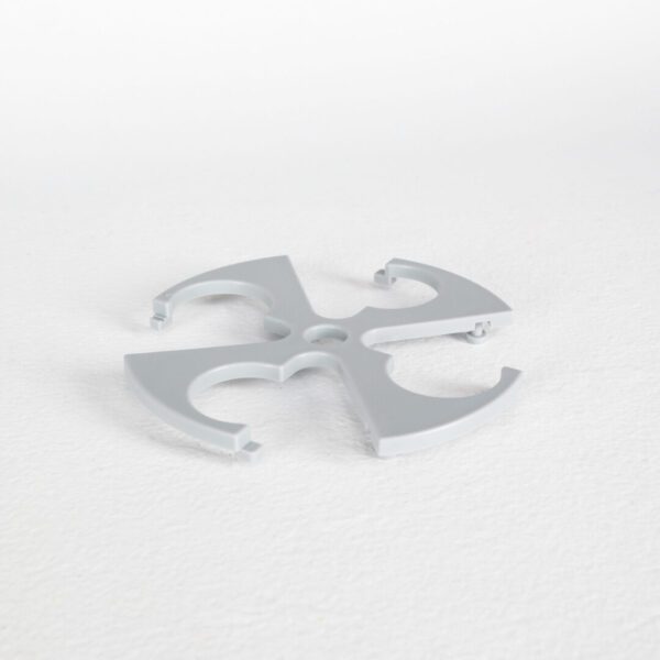 Sentence with replaced product name: Gray plastic object with four cutouts, shaped like an abstract butterfly, placed on a white textured surface.