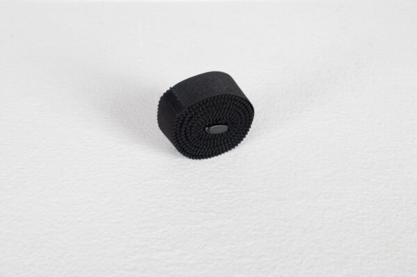 A rolled-up black Velcro strap on a white textured background.