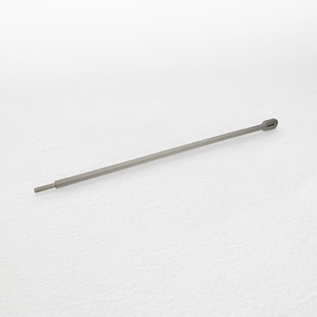 The Spine, a long gray metal rod with a slotted end, lying on a white surface.