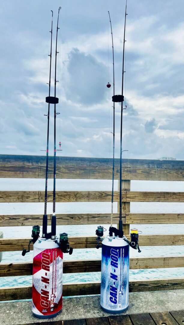 Two fishing rods mounted on propane tanks against a backdrop of a cloudy sky and distant landscape, seen from a wooden deck.